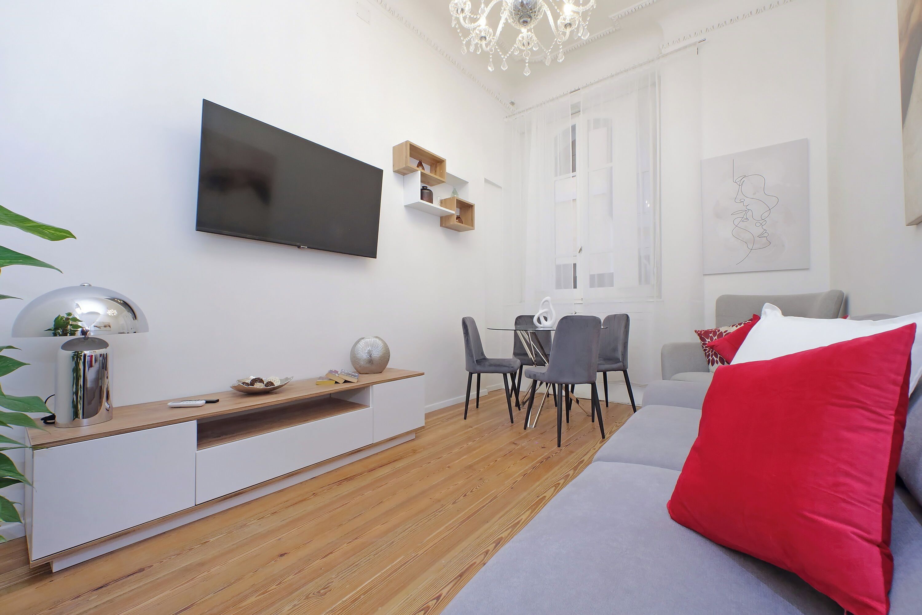 A modern living room with a flat-screen TV, a dining area with a glass table, and a sofa with red cushions.