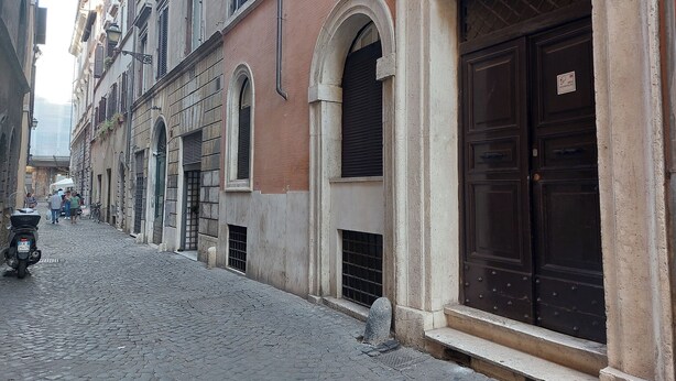 Una calle empedrada flanqueada por edificios históricos, destacando una puerta de madera oscura y un bolardo de piedra.