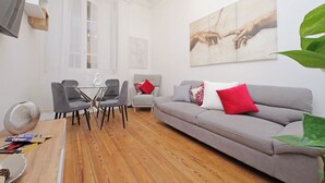 Una sala de estar moderna con un sofá gris, cojines rojo y blanco, una mesa de comedor con sillas y un cuadro abstracto grande en la pared.
