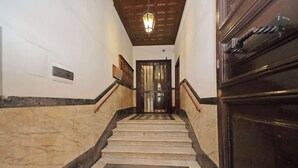 Una escalinata de mármol con un suelo de diseño geométrico que conduce a una puerta con portón metálico.