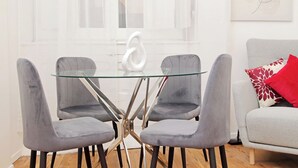 Un comedor moderno con una mesa de vidrio y cuatro sillas grises tapizadas.