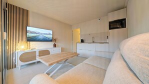 A modern, compact living space with a flat-screen TV mounted on the wall, a wooden dining table, a sofa, and a kitchenette area. - Seaside, cosy apartment + parking, facing Santa Lucia harbour (Saint-Raphaël)