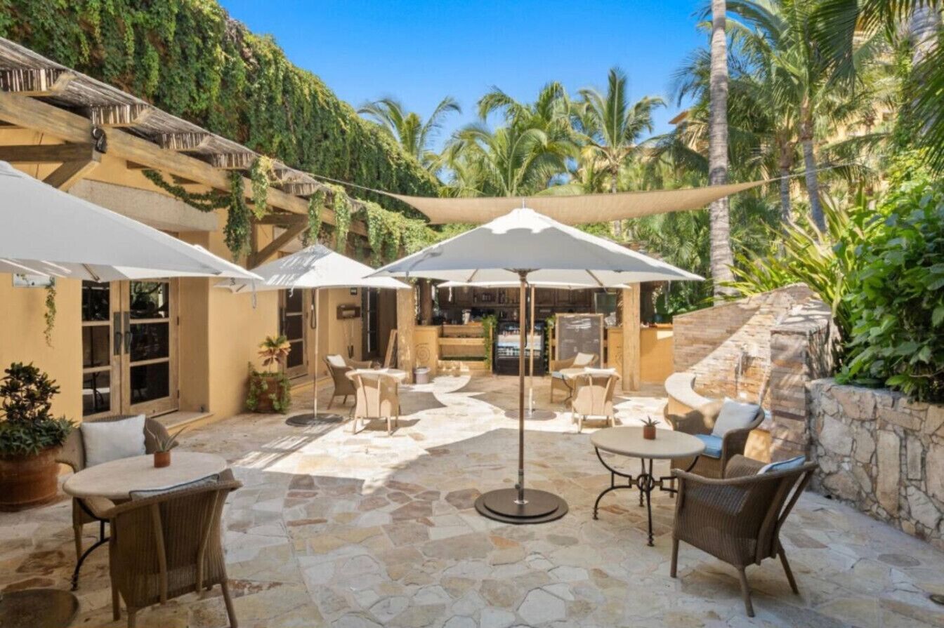An outdoor patio with stone flooring, white umbrellas, wicker furniture, and a stone wall.