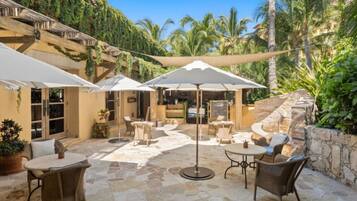 An outdoor patio with stone flooring, white umbrellas, wicker furniture, and a stone wall.