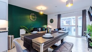 Een moderne eetruimte met een houten tafel voor vier personen, een groene accentmuur, een grote wandklok en uitzicht op de stad door het raam.