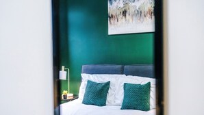 Een bed met een blauw hoofdeinde, wit beddengoed en groene kussens.