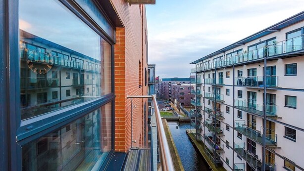 Een modern gebouw met grote ramen, een bakstenen gevel en een smalle waterweg tussen de gebouwen.