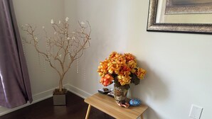 Une table en bois, sur laquelle se trouve un vase de fleurs et un arbre décoratif, le tout adossé à un mur blanc.