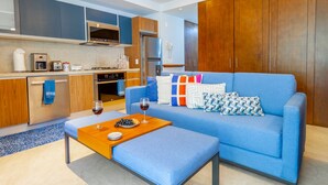 A modern living room with a blue sofa, wooden cabinets, and a kitchen area with appliances. - Sunny Studio in Romantic Zone. Steps to Beach. (Puerto Vallarta)