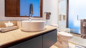 A modern bathroom with a large mirror, a round sink, a toilet, and a glass shower enclosure. - Sunny Studio in Romantic Zone. Steps to Beach. (Puerto Vallarta)