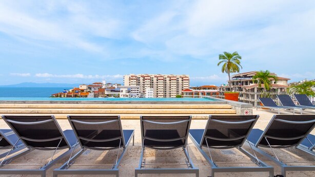 A beachside hotel with a pool, lounge chairs, and a view of the ocean and buildings. - Sunny Studio in Romantic Zone. Steps to Beach. (Puerto Vallarta)
