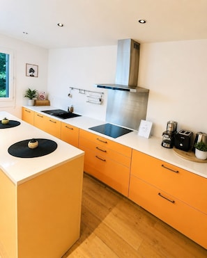 A modern kitchen with a central island, a stainless steel range hood, and a window with a view of greenery.
