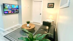 Ein modernes Wohnzimmer mit einem wandmontierten Flachbildfernseher, einem runden Couchtisch mit Pflanze, einer Ledersofa und einer Lampe.