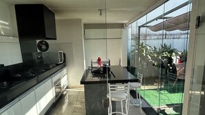 A modern kitchen with a large island, white bar stools, and a view of a green lawn through large glass doors. - Large house with floor (São Paulo)