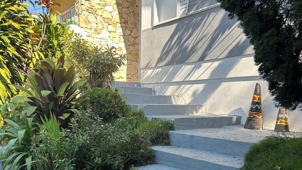 A set of concrete steps leading up to a stone wall, surrounded by lush greenery and decorative cones. - Large house with floor (São Paulo)