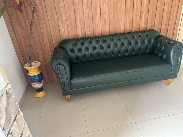 Un sofá de cuero verde oscuro con detalles capitonados frente a una pared de paneles de madera, acompañado por un jarrón decorativo con una planta.