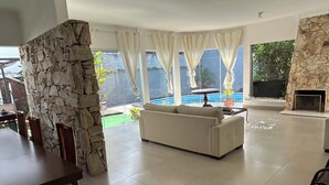 A spacious living area with a white sofa, stone wall, and a view of a swimming pool. - Large house with floor (São Paulo)