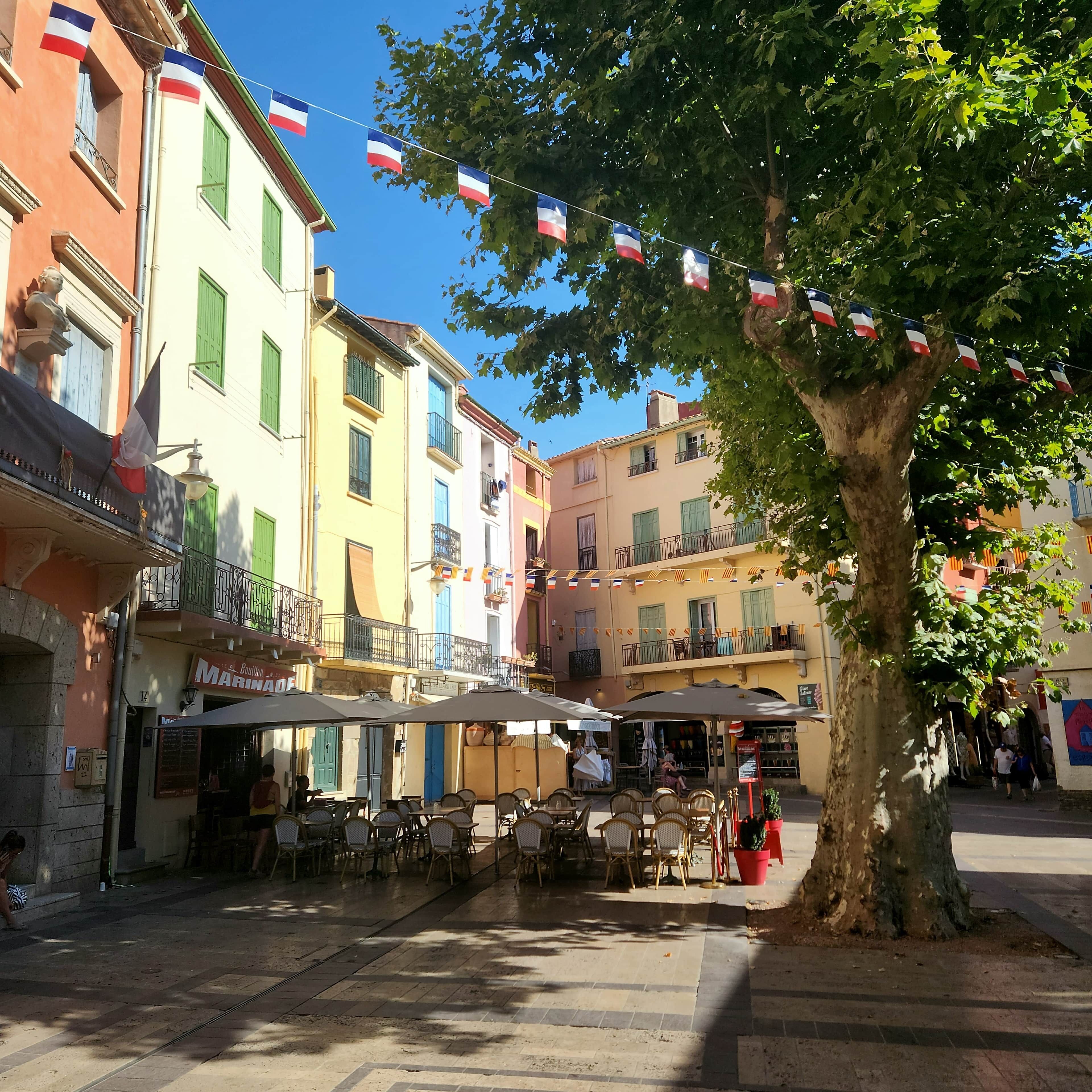 A street with outdoor seating, a tree, and buildings with balconies.