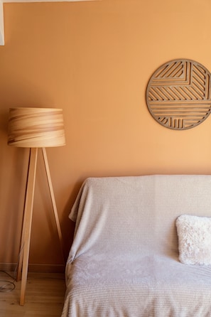 Une pièce avec un lampadaire en bois, un élément décoratif rond fixé au mur, un canapé beige et un coussin blanc.