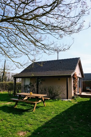 A house with a sloped roof, a wooden picnic table, and a grassy yard.