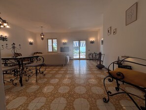 Amplia sala de estar con piso estampado, un sofá, una mesa de comedor con sillas y un televisor.