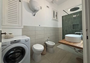 Ett modernt badrum med tvättmaskin, toalett, bidé och ett stort handfat.