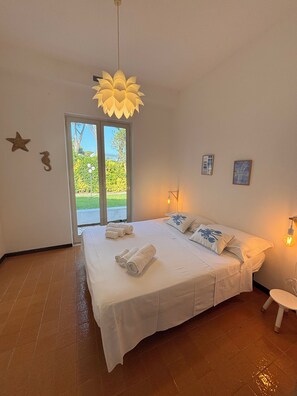 A bedroom with a bed, towels, a hanging light fixture, and a view through a sliding door.