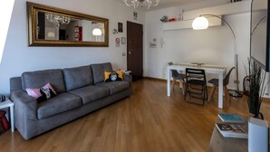 A modern living room with a grey sofa, a dining table with chairs, a chandelier, and a large mirror on the wall. - Acasadigiò B&B - 400 meters from the Metro stop and 15 minutes from the center of Rome (Roma)