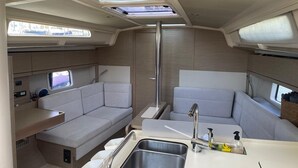 A compact kitchenette with a sink, faucet, and storage. There are two seating areas with cushions, a window, and a ceiling skylight.