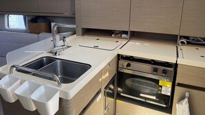 A compact kitchen with a sink, two drawers, a stove, and a window above the sink.