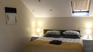 A bedroom with a bed, two bedside tables, a window, and a ceiling light.