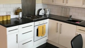 A compact kitchen with a stove, oven, and sink, white cabinets, and a black countertop.