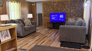 A living room with two sofas, a TV, a wooden wall, and a stone wall.