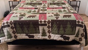 A bed with a quilt, two bedside tables, and two wall-mounted lamps.