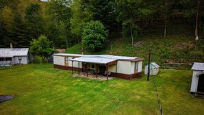 A mobile home with a covered patio, surrounded by a grassy yard and trees.