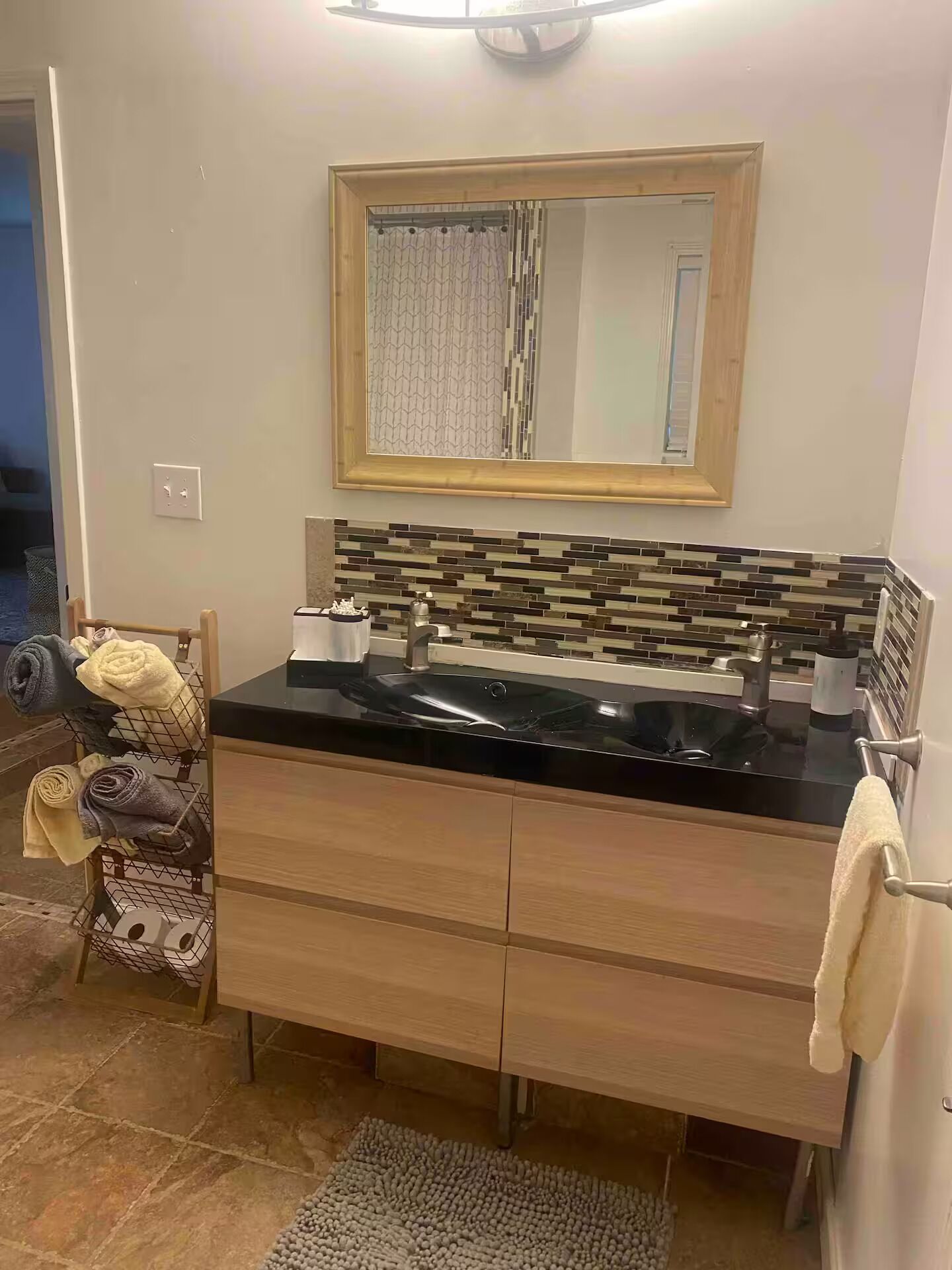 A bathroom with a black sink, wooden vanity, and a tiled backsplash.