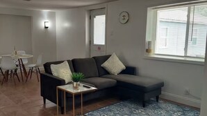 Ein Wohnzimmer mit einem dunkelgrauen Sofa, weißen Sesseln, einem kleinen runden Tisch und einem blau gemusterten Teppich.