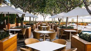 Un espace extérieur aménagé pour les repas, avec des meubles en osier, des parasols blancs et une piscine en arrière-plan.