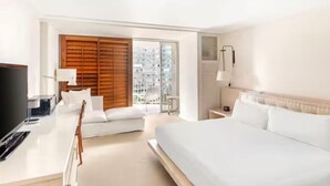 Une chambre d’hôtel moderne dotée d’un grand lit, d’un bureau avec un ordinateur, d’une télévision et offrant une vue sur la ville grâce à de grandes fenêtres.