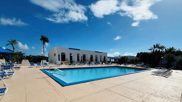 A swimming pool with blue water, surrounded by lounge chairs and umbrellas, with a building in the background. - Enjoy Passport to Paradise! (Christiansted)