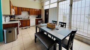 A kitchen with wooden cabinets, a dining table with chairs, and a trash bin. - Enjoy Passport to Paradise! (Christiansted)