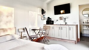 A modern hotel room with a bed, a desk, a kitchenette, and a TV.