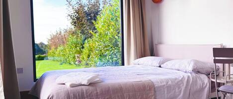 A bedroom with a large window, a bed, a desk, and a chair.