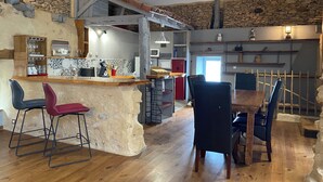 A rustic kitchen with stone walls, wooden beams, and a bar area with stools.