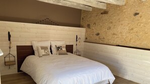 A bedroom with a wooden headboard, a bed with white bedding, and a stone wall.