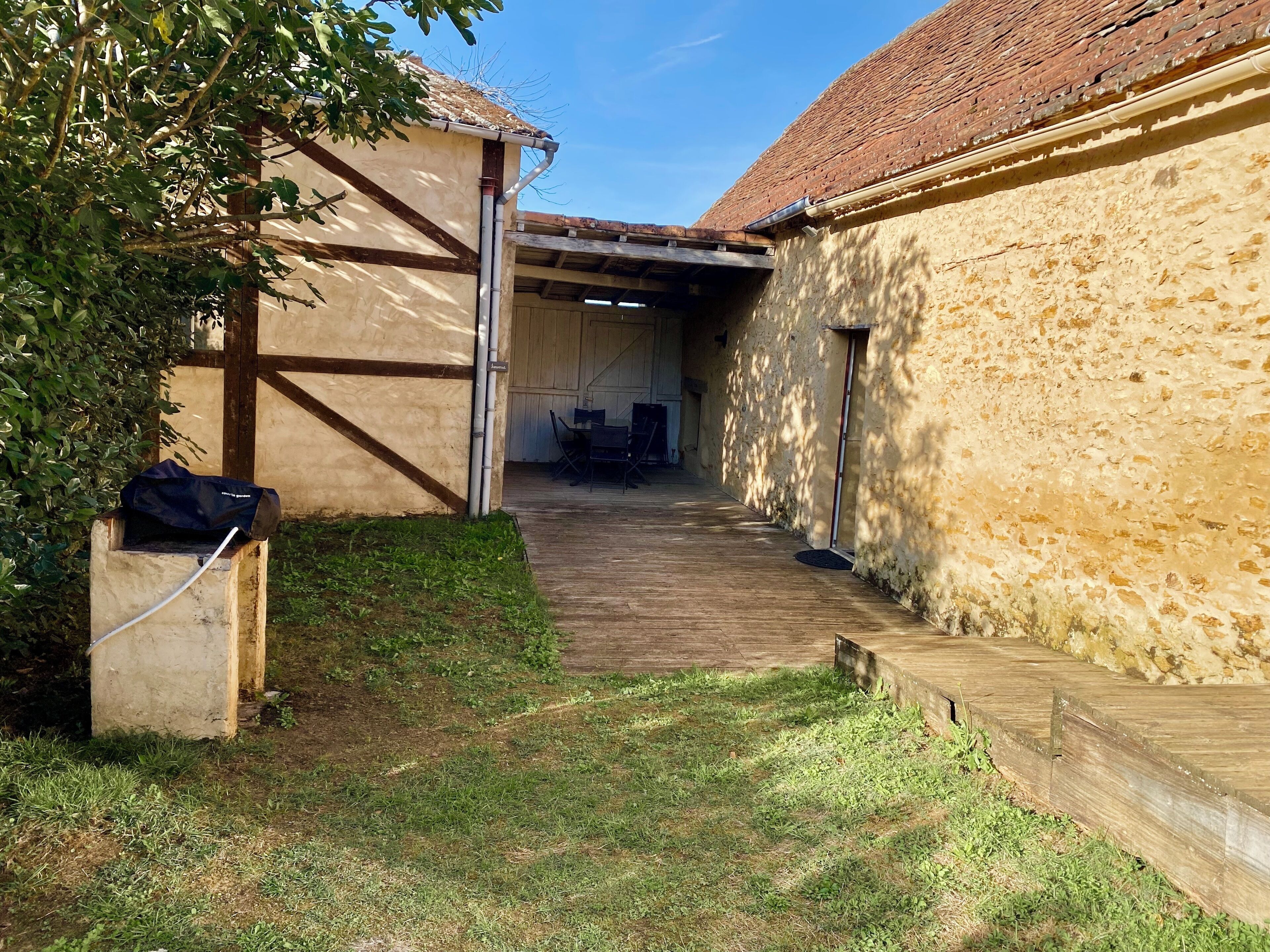 Un espacio al aire libre techado con piso de madera, una estructura de concreto a la izquierda y un muro de piedra a la derecha.