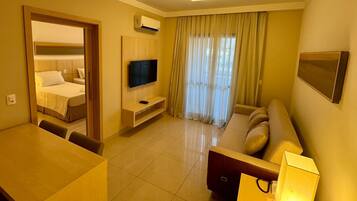 Quarto de hotel com cama, televisão, sofá, secretária e luminária.