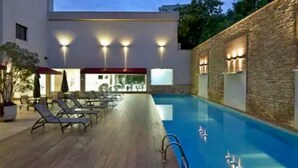 Un espace piscine avec des chaises longues, une terrasse en bois et un mur en pierre.