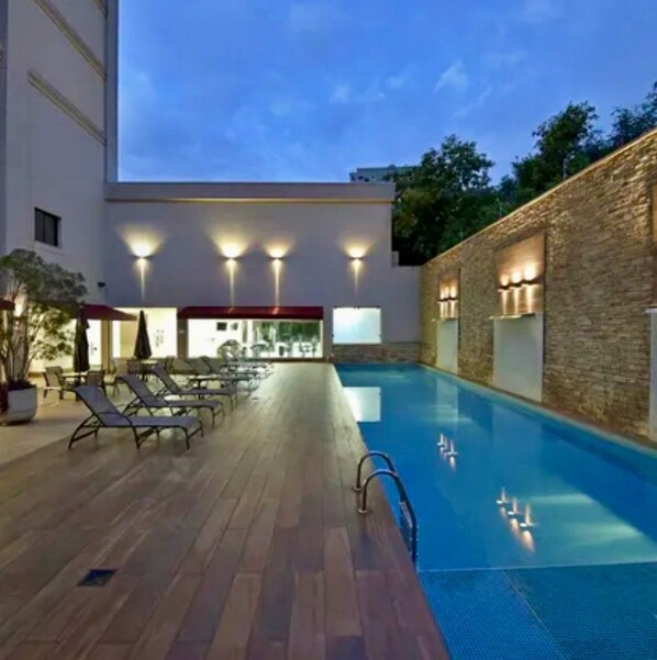 A pool area with lounge chairs, a wooden deck, and a stone wall.
