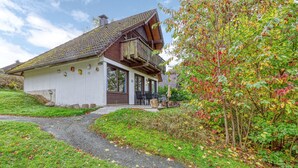 Ein zweistöckiges Haus mit geneigtem Dach, einem Balkon und einer kleinen Veranda mit Sitzgelegenheit.
